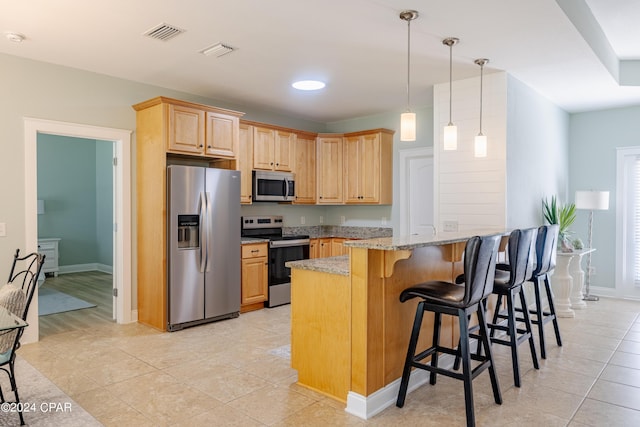 kitchen with light stone counters, a breakfast bar area, visible vents, appliances with stainless steel finishes, and a peninsula