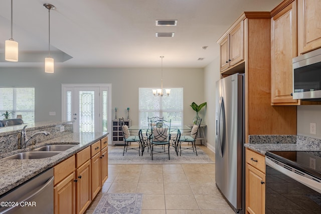 kitchen with stainless steel appliances, hanging light fixtures, a sink, and light stone countertops