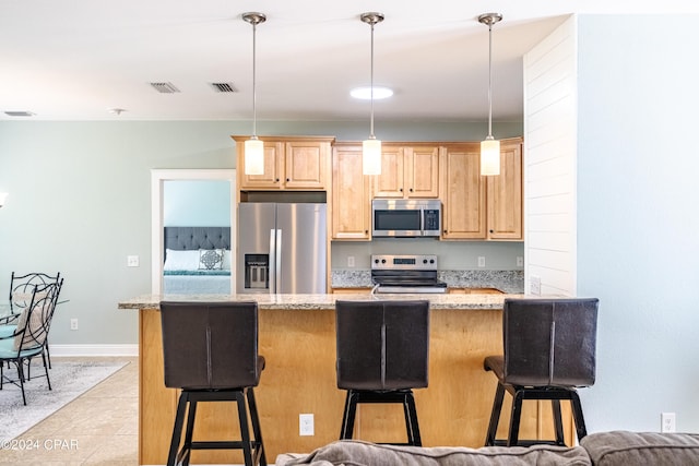 kitchen with pendant lighting, appliances with stainless steel finishes, light brown cabinets, light stone countertops, and a kitchen bar