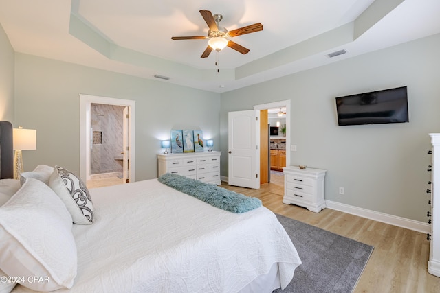 bedroom featuring a raised ceiling, baseboards, connected bathroom, and light wood finished floors