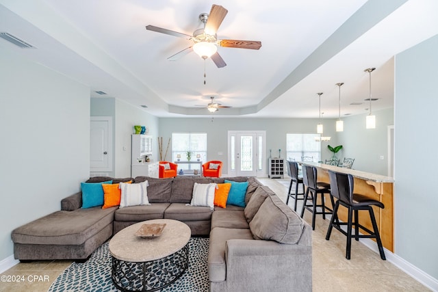 living room with a raised ceiling and ceiling fan with notable chandelier