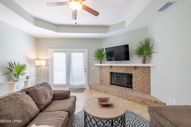 living room featuring light tile patterned floors, ceiling fan, a brick fireplace, and visible vents