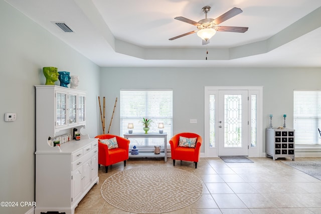 living area featuring light tile patterned floors, a raised ceiling, visible vents, and a healthy amount of sunlight