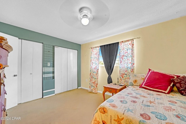 bedroom with a textured ceiling, carpet floors, ceiling fan, and two closets