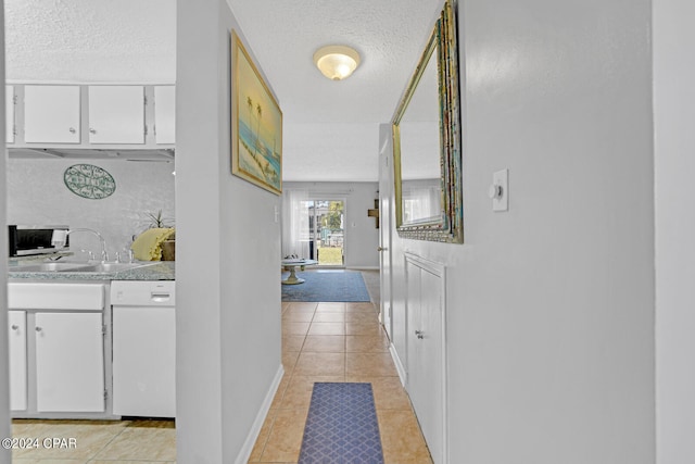 corridor with a textured ceiling, sink, and light tile patterned flooring