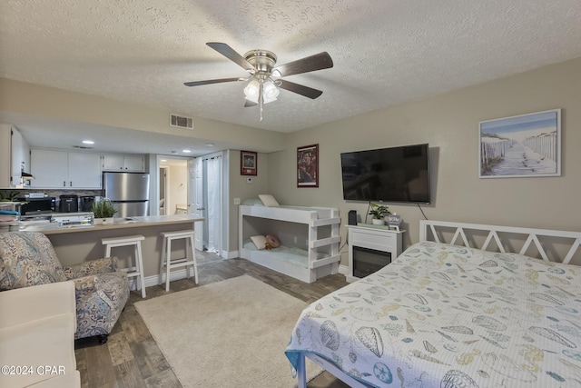 bedroom with a textured ceiling, ceiling fan, stainless steel refrigerator, and hardwood / wood-style flooring