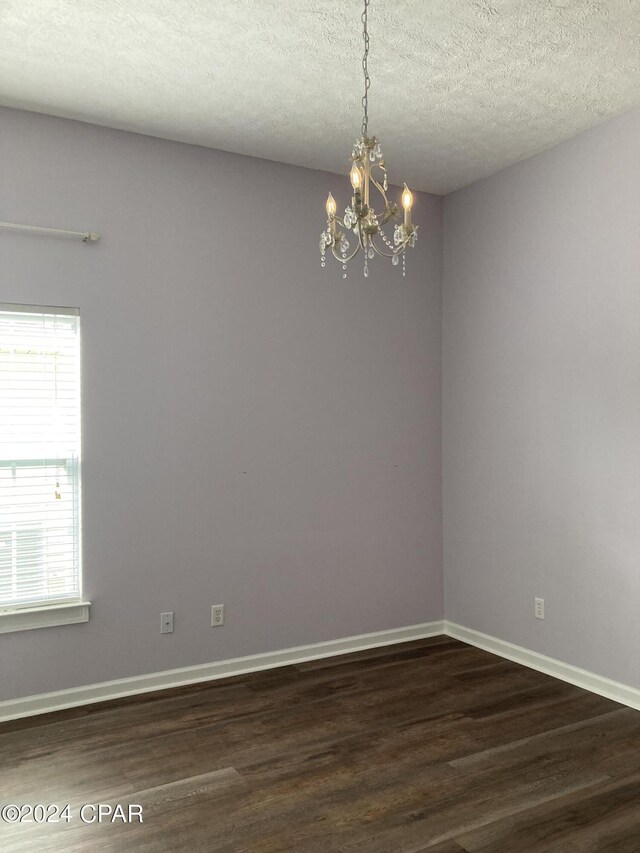 unfurnished room featuring dark hardwood / wood-style floors, a textured ceiling, and an inviting chandelier