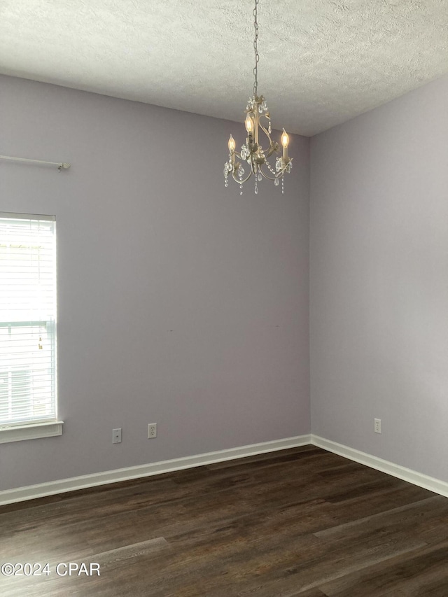 empty room featuring dark wood-style flooring, a textured ceiling, baseboards, and an inviting chandelier