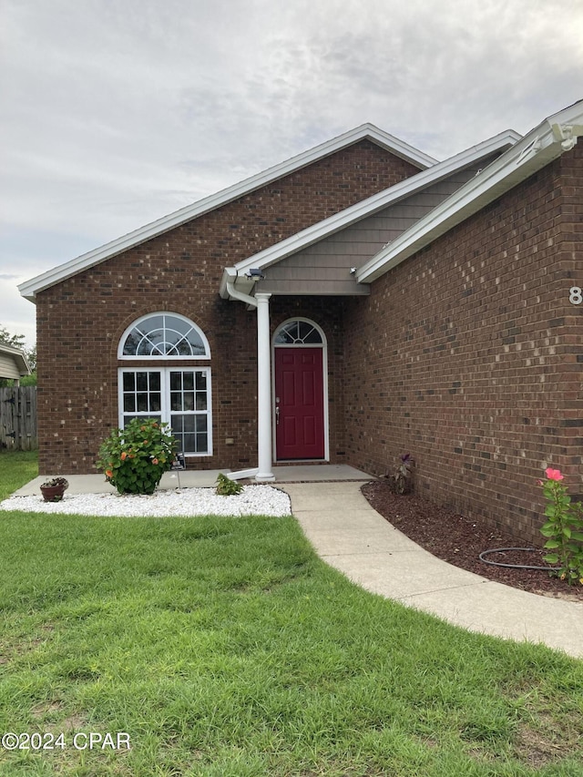 doorway to property featuring brick siding and a lawn