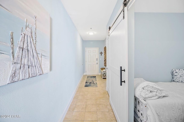 corridor featuring light tile patterned floors, baseboards, and a barn door