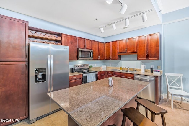 kitchen featuring stainless steel appliances, a sink, a kitchen island, light stone countertops, and a kitchen bar