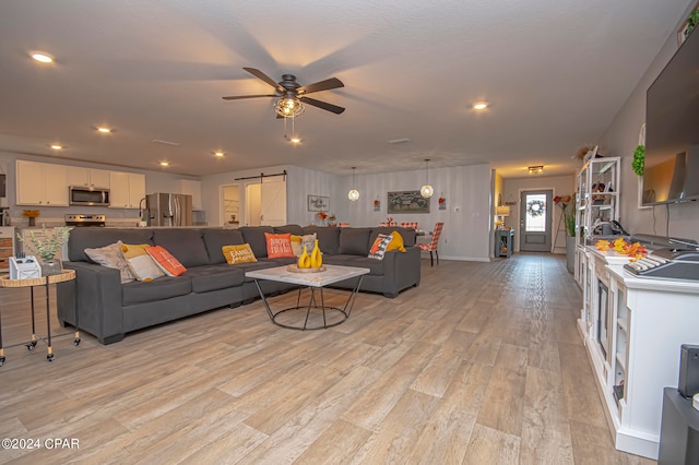 living room featuring ceiling fan, a barn door, and light hardwood / wood-style floors