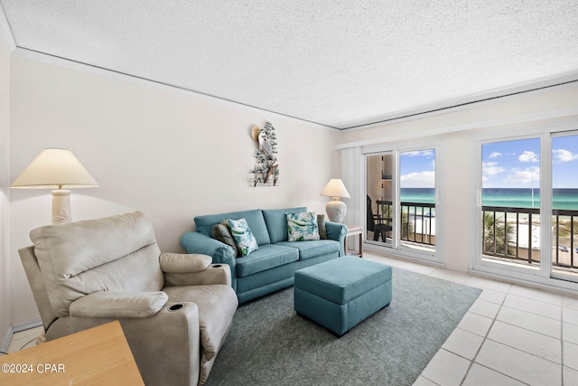 tiled living room featuring a view of the beach, a water view, a textured ceiling, and crown molding