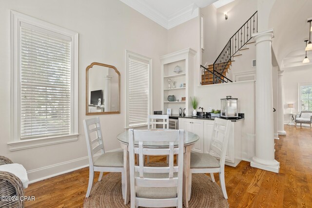 dining room featuring wood-type flooring, crown molding, and decorative columns