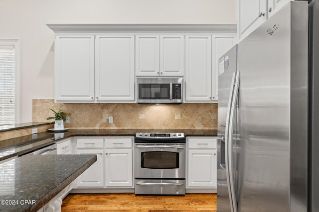 kitchen with appliances with stainless steel finishes, dark stone counters, light wood-type flooring, and white cabinets