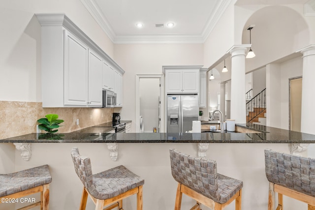 kitchen featuring appliances with stainless steel finishes, decorative columns, white cabinetry, and kitchen peninsula