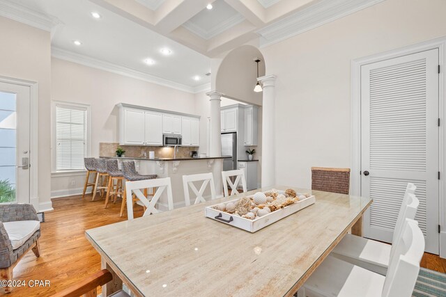 dining area featuring light wood-type flooring, beam ceiling, coffered ceiling, crown molding, and ornate columns