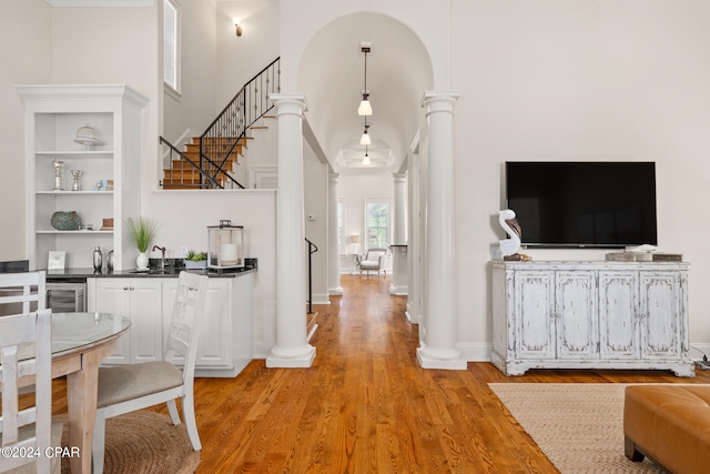 interior space featuring light hardwood / wood-style flooring, a towering ceiling, hanging light fixtures, and ornate columns