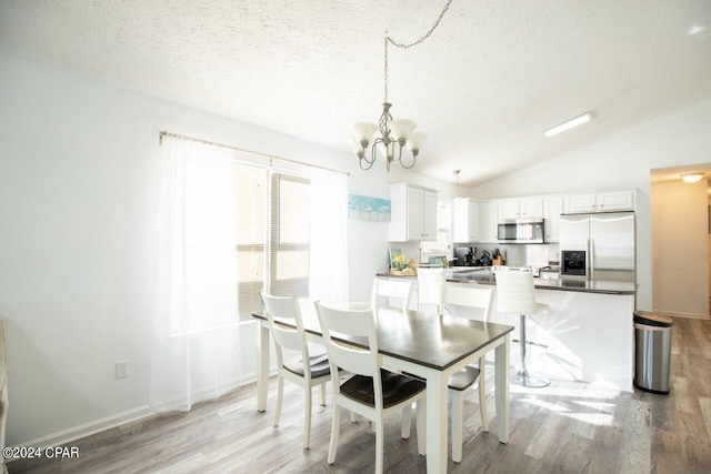 dining room featuring lofted ceiling, an inviting chandelier, a textured ceiling, and light hardwood / wood-style flooring