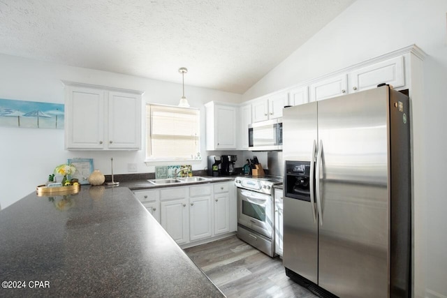 kitchen featuring vaulted ceiling, hanging light fixtures, stainless steel appliances, sink, and light wood-type flooring