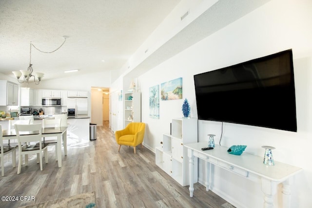 living room with lofted ceiling, light wood-type flooring, a chandelier, and a textured ceiling