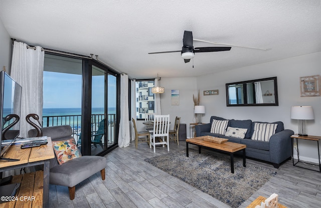 living room featuring light hardwood / wood-style floors, a water view, ceiling fan, and a wall of windows