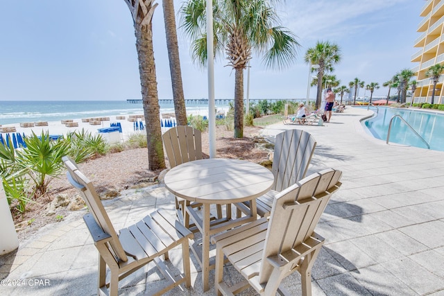 view of patio / terrace with a community pool, a water view, and a view of the beach