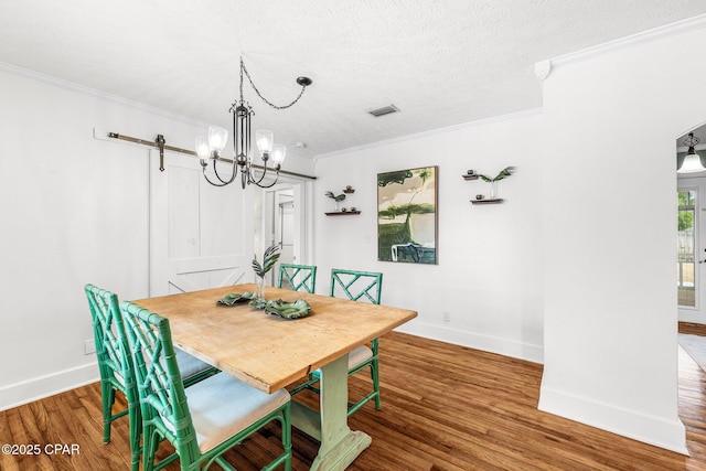 dining space with wood-type flooring, a chandelier, a textured ceiling, ornamental molding, and a barn door