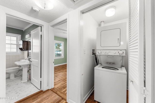 clothes washing area with stacked washer and clothes dryer, hardwood / wood-style floors, a textured ceiling, and a wealth of natural light