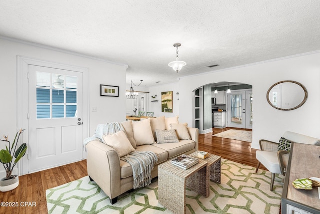 living room featuring ornamental molding, a chandelier, a textured ceiling, and light wood-type flooring