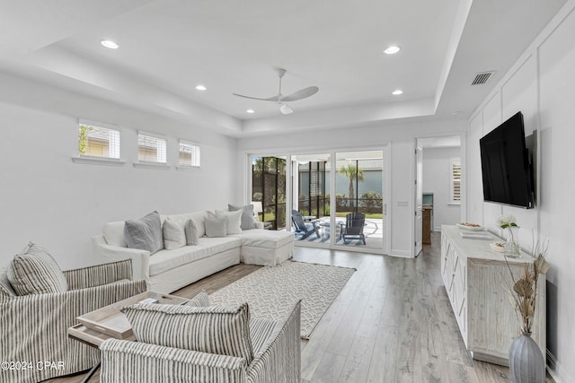 living room featuring light hardwood / wood-style floors, a tray ceiling, and ceiling fan