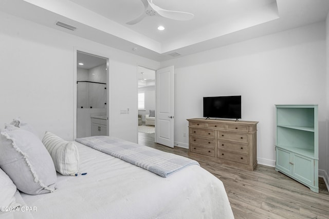 bedroom with ceiling fan, hardwood / wood-style flooring, a tray ceiling, and ensuite bath