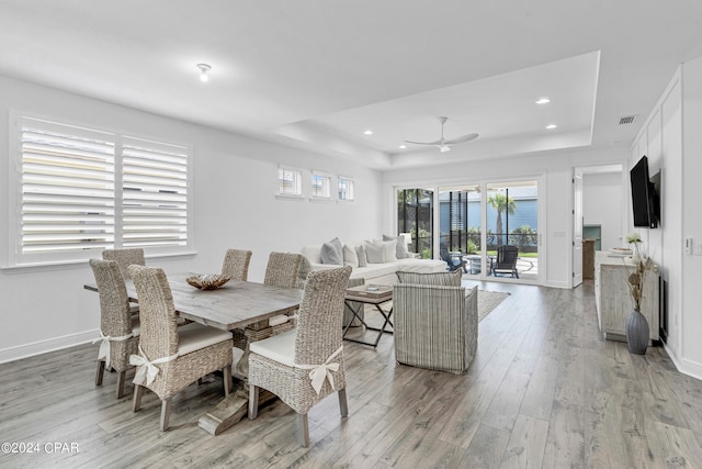 dining room featuring ceiling fan, light wood-type flooring, and a tray ceiling