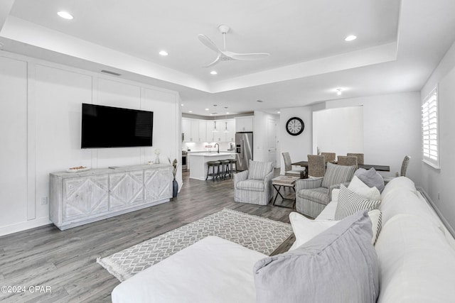 living room featuring ceiling fan, light hardwood / wood-style flooring, and a tray ceiling