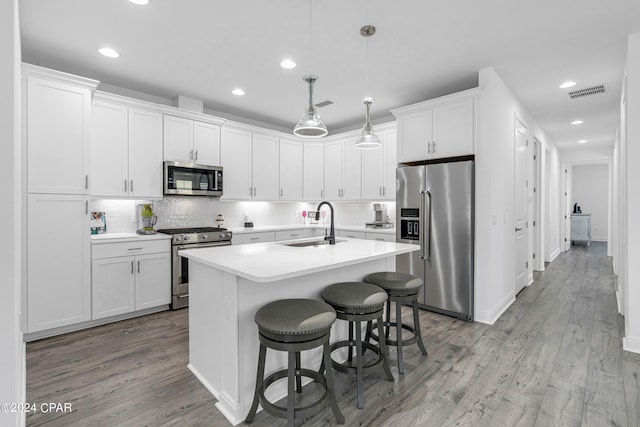 kitchen with light hardwood / wood-style floors, white cabinets, stainless steel appliances, decorative light fixtures, and sink