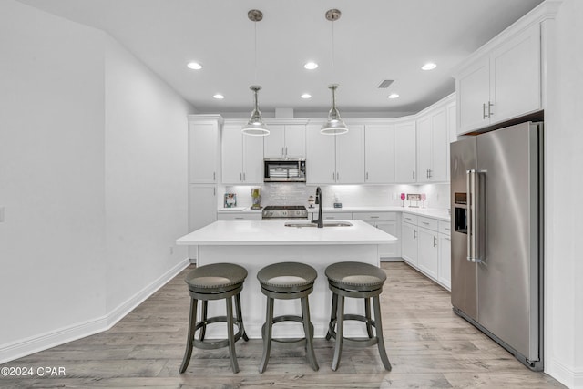 kitchen featuring pendant lighting, sink, white cabinets, a center island with sink, and appliances with stainless steel finishes