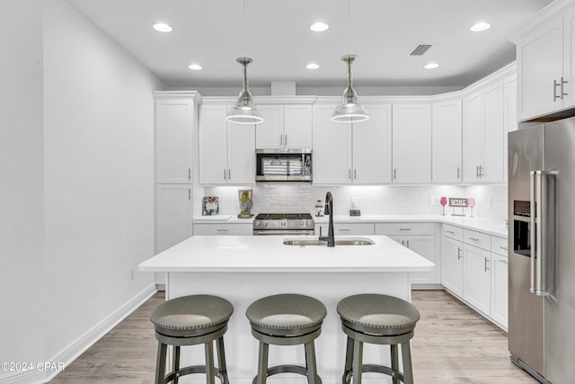 kitchen with white cabinetry, premium appliances, pendant lighting, and an island with sink