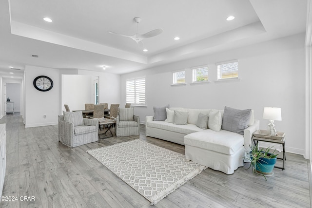 living room featuring a raised ceiling, ceiling fan, and light hardwood / wood-style flooring