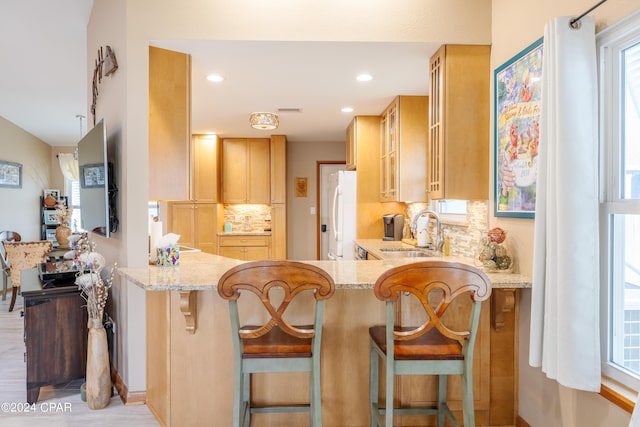 kitchen with light stone counters, tasteful backsplash, a sink, and freestanding refrigerator