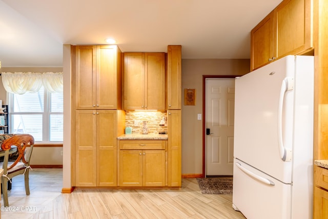 kitchen featuring light wood finished floors, baseboards, light stone counters, freestanding refrigerator, and backsplash