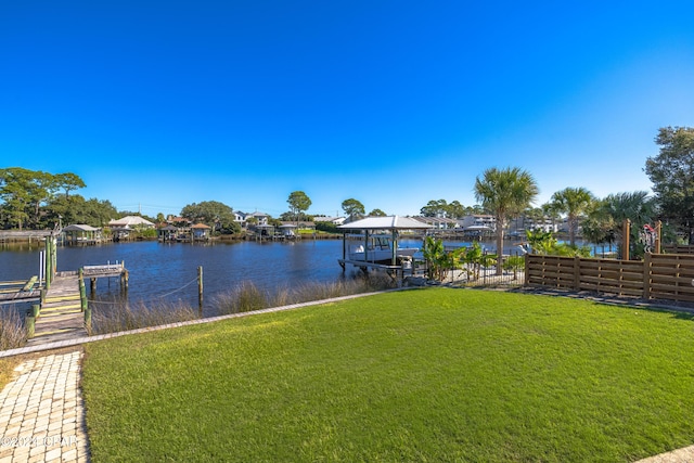 dock area with a lawn, a water view, boat lift, and fence