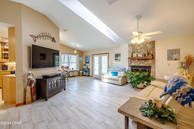 living area featuring a ceiling fan, light wood-type flooring, french doors, and a stone fireplace