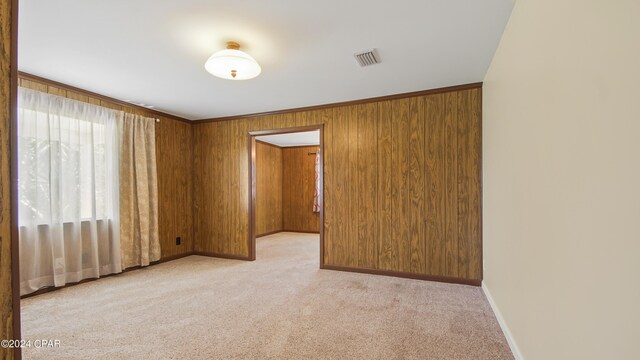 unfurnished room with plenty of natural light, light carpet, and wooden walls