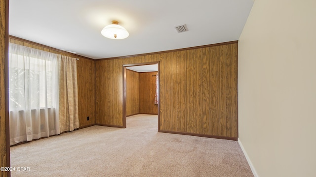 unfurnished room with baseboards, wooden walls, visible vents, and light colored carpet