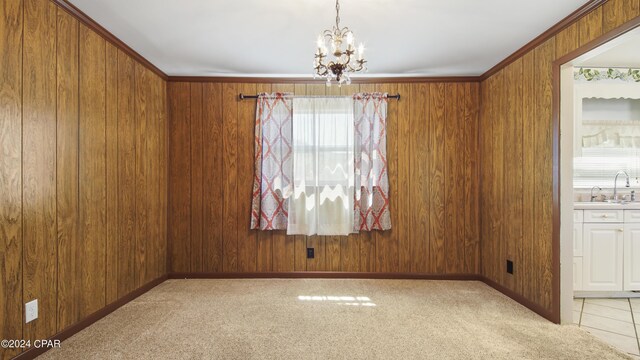 carpeted spare room with wooden walls, sink, a notable chandelier, and ornamental molding