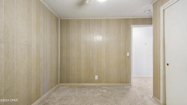 empty room featuring carpet, wooden walls, and crown molding