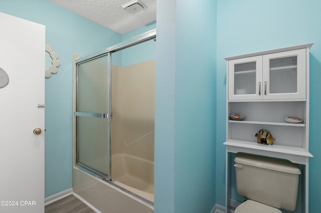 bathroom featuring a textured ceiling, toilet, wood-type flooring, and enclosed tub / shower combo