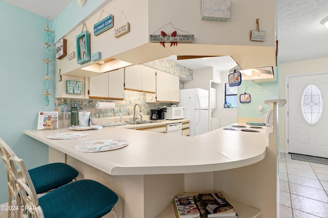 kitchen featuring a textured ceiling, kitchen peninsula, sink, and white appliances