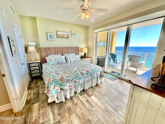 bedroom with a water view, a textured ceiling, wood-type flooring, access to exterior, and ceiling fan