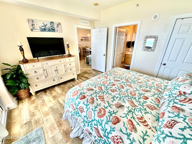 bedroom with a textured ceiling, light hardwood / wood-style flooring, and ensuite bathroom